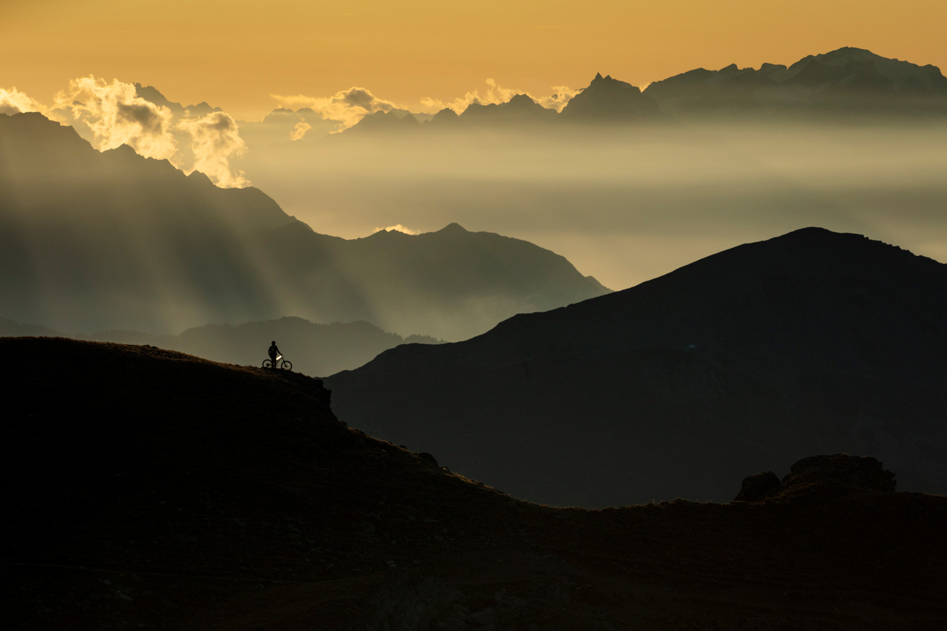 Silhouette eines Mountainbikers vor Bergkulisse im Sonnenuntergang.