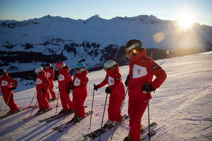 Skilehrer stehen auf der Piste und hören jemanden zu.