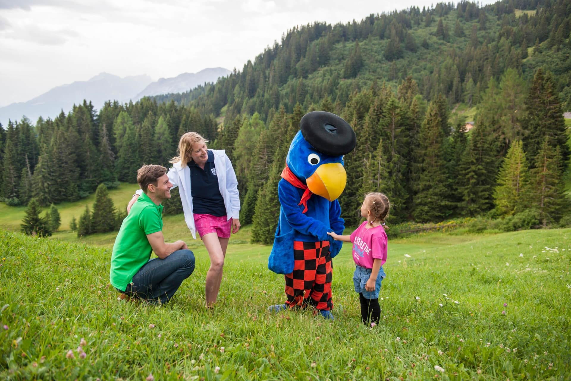 Familie trifft ein verkleidetes Maskottchen auf einer Wiese.