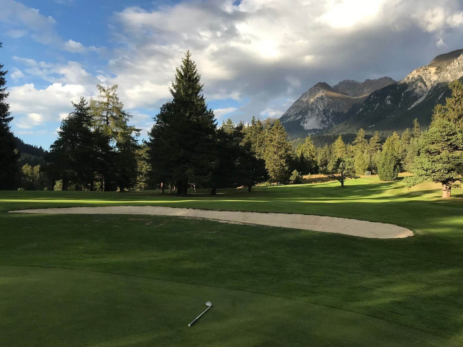 Golfplatz mit Bunker vor einer Berglandschaft.