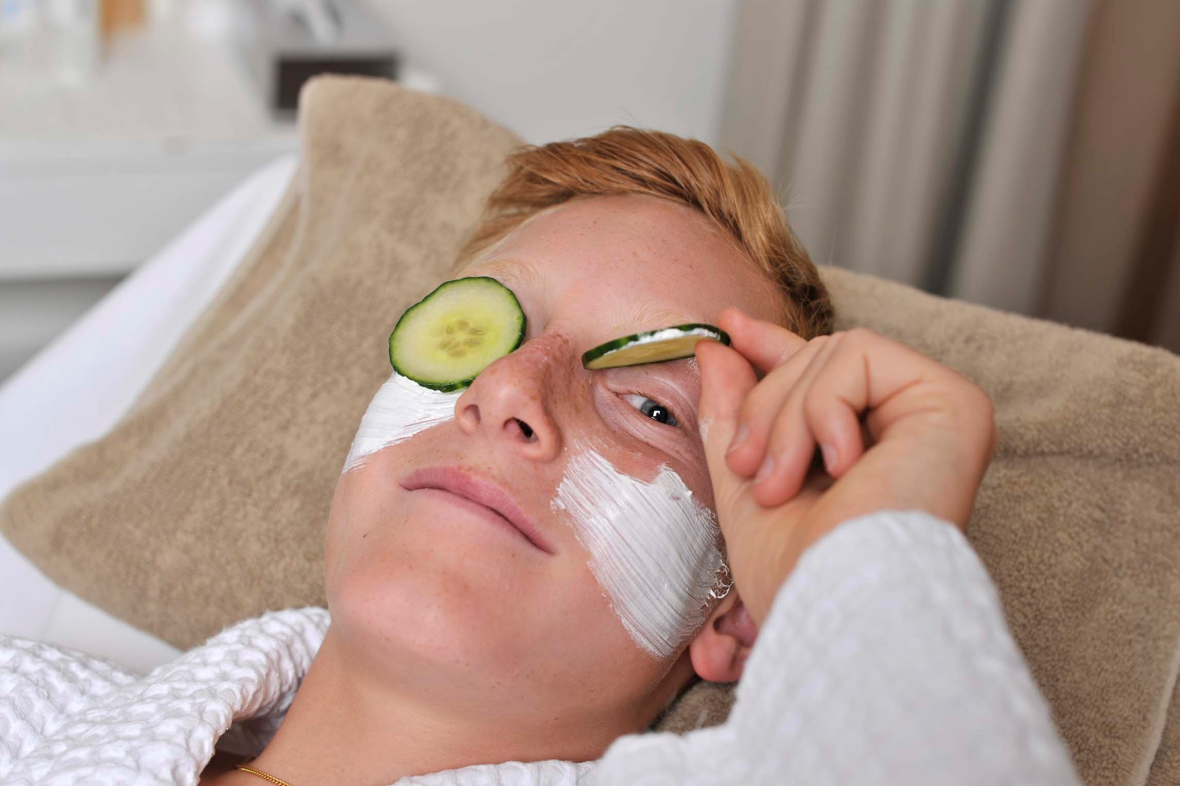 Jugendlicher mit Gesichtsmaske und Gurkenscheiben auf den Augen.