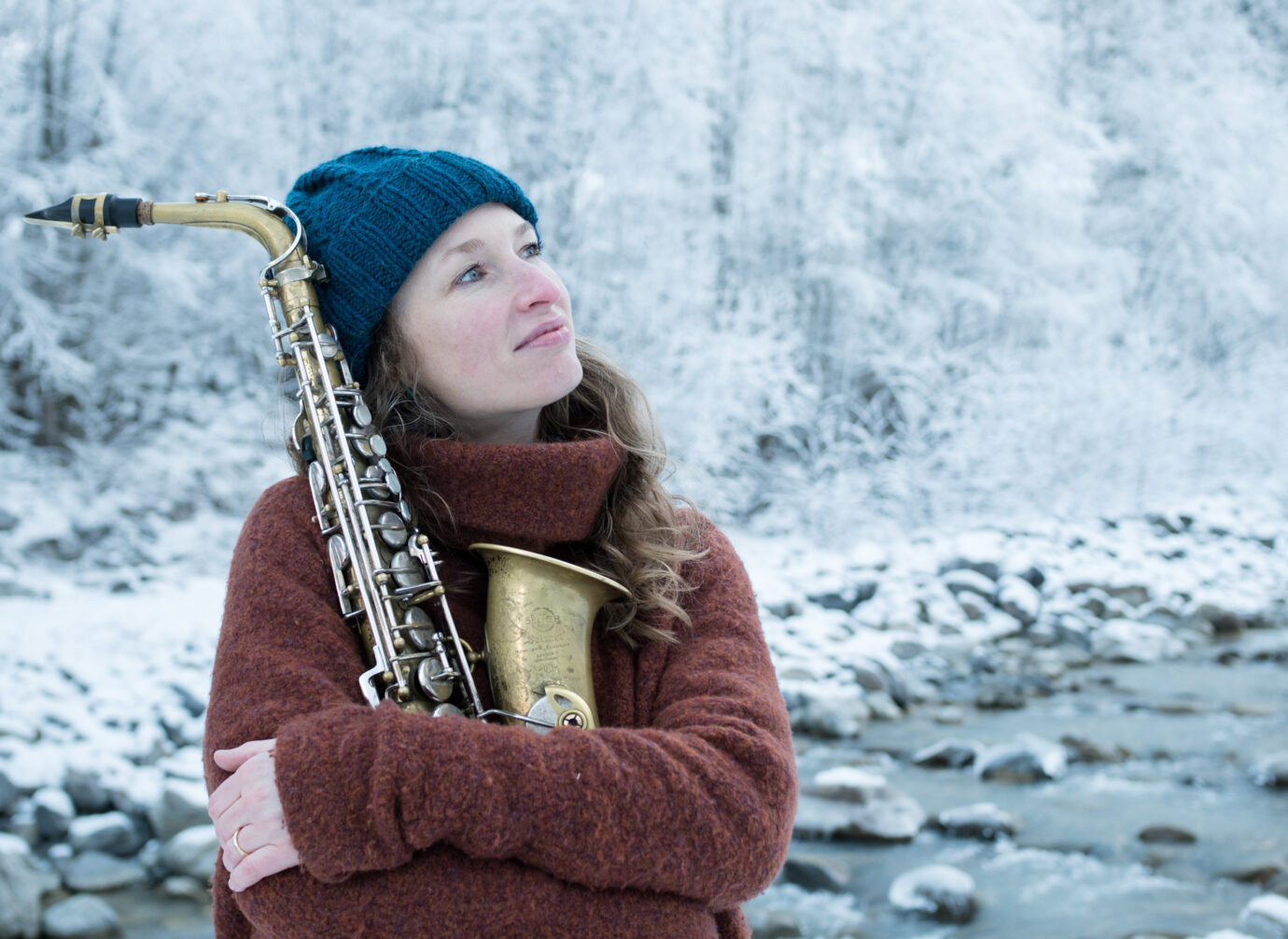 Frau im Winter mit Saxofon vor verschneiter Landschaft am Fluss.