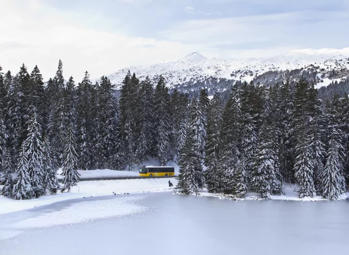 Schweizer Postauto welches durch die winterliche Landschaft fährt.