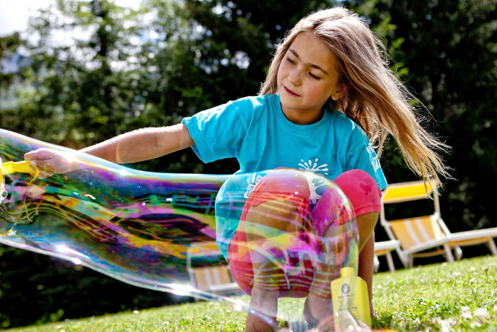 Kind im Garten die mit eine riesige Seifenblase zieht.