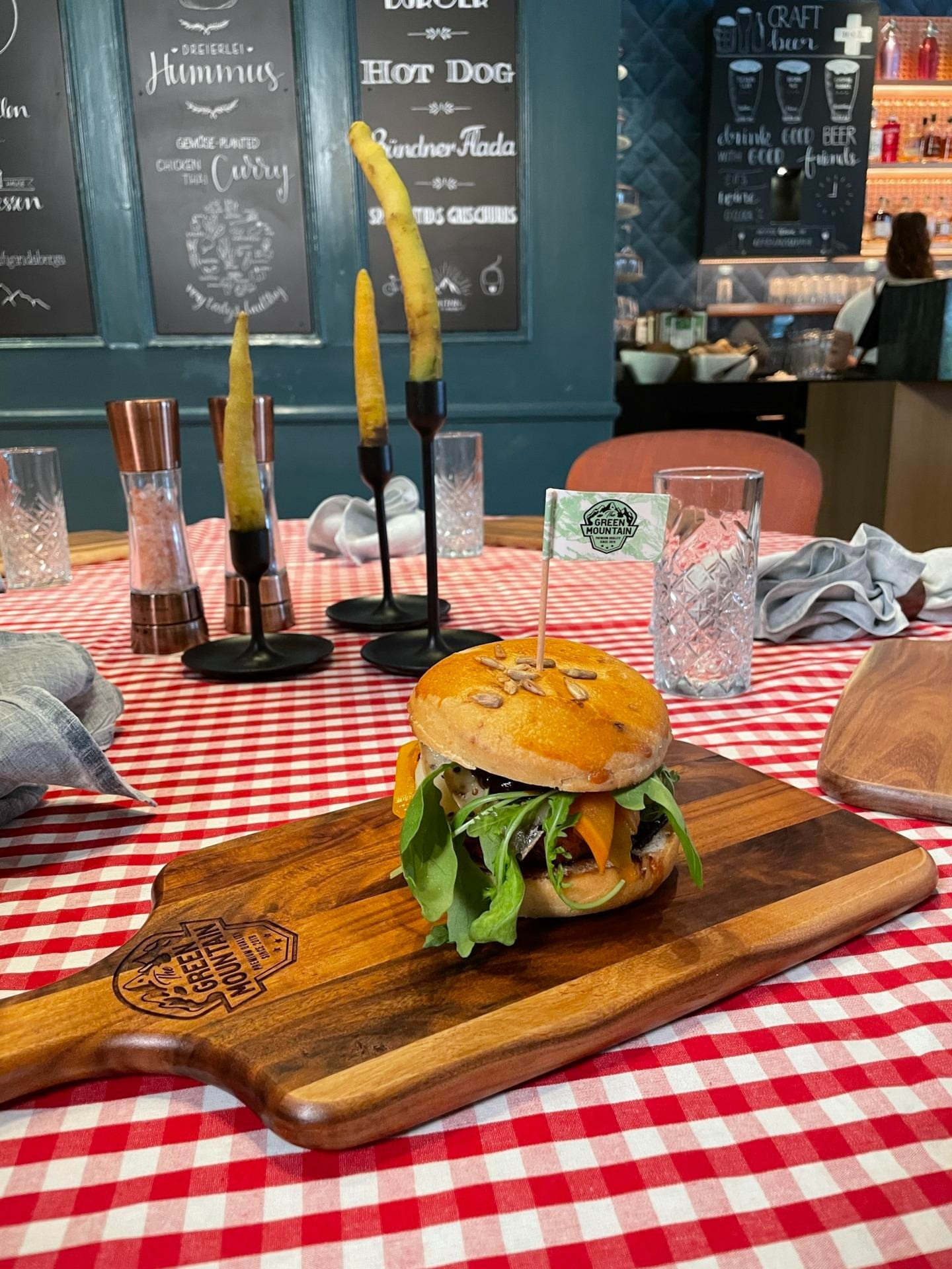 Gedeckter Tisch mit Kerzen und Gläsern und in der Mitte ein Burger mit Gemüse und mit einem Fähnchen in der Mitte.