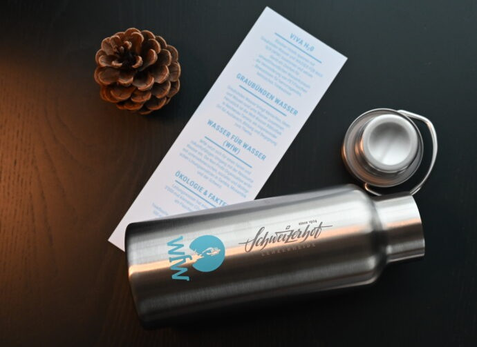 .Wasserflasche und Tannenzapfen sowie Infoblatt auf einem Tisch