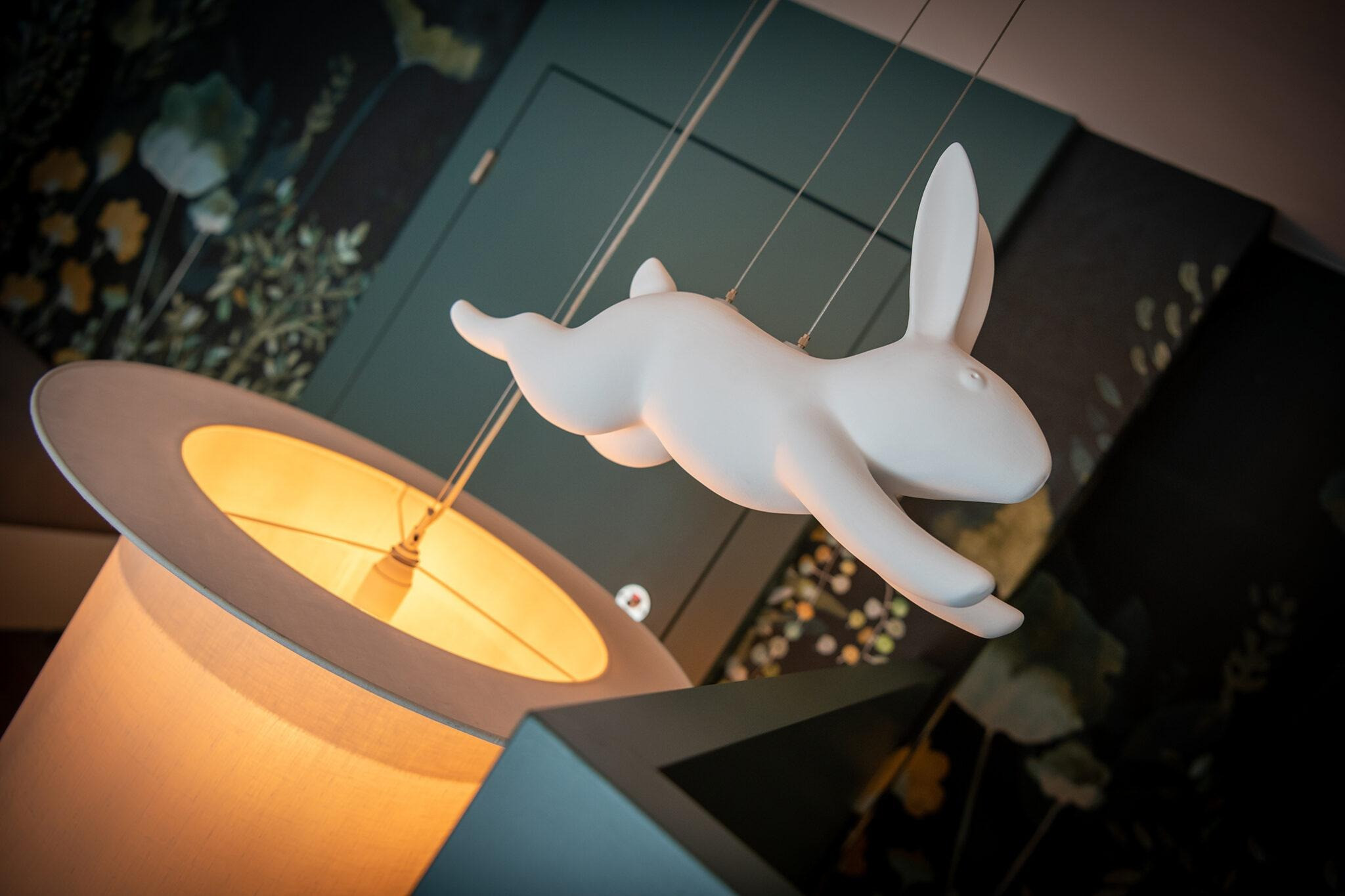 Hängelampe mit einer fliegenden Hasenfigur über einem warm leuchtenden Lampenschirm.