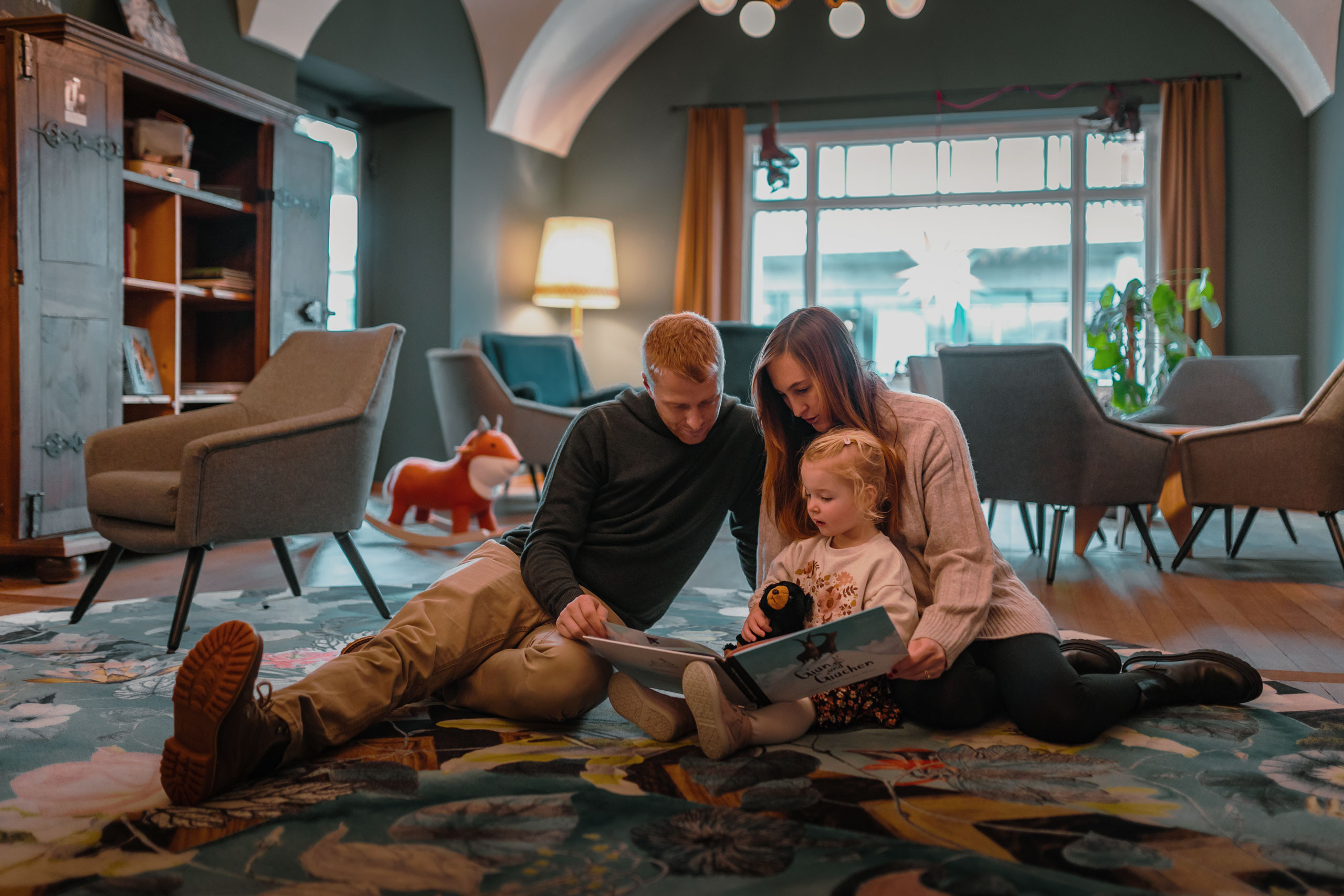 Eine Familie sitzt auf dem Boden und schaut gemeinsam ein Kinderbuch an.