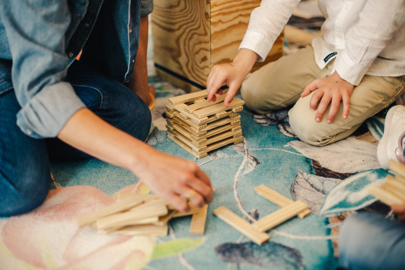 Kinder und eine erwachsene Person bauen gemeinsam einen Turm aus Holzstäbchen.
