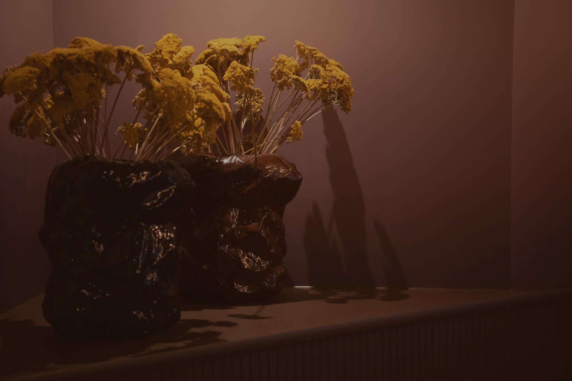 Zwei dunkle Vasen mit getrockneten Blumen stehen auf einer Ablage.