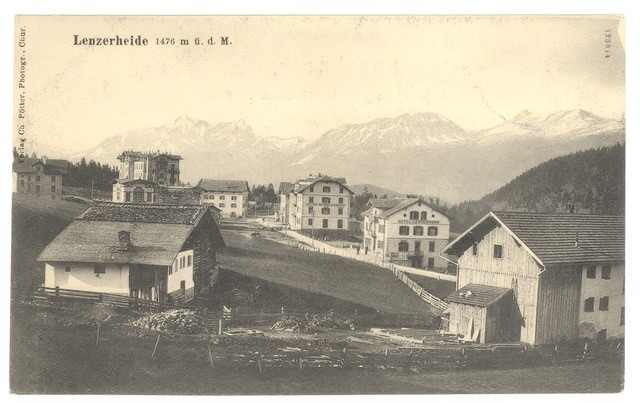 Historische Ansicht von Lenzerheide mit alten Häusern, Wiesen und Bergen im Hintergrund.
