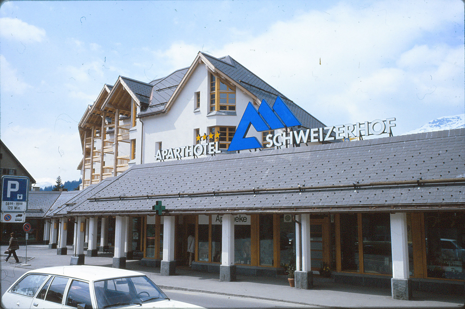 ussenansicht des Aparthotel Schweizerhof in Lenzerheide mit markantem Dach, grossem Schriftzug und Geschäftszeile.