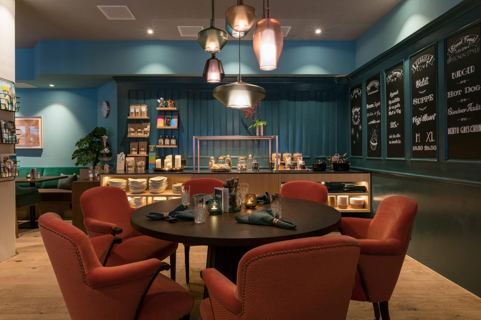 Ein runder gedeckter Tisch mit moderner Lampe darüber und im Hintergrund eine Selbstbedienungs-Theke.