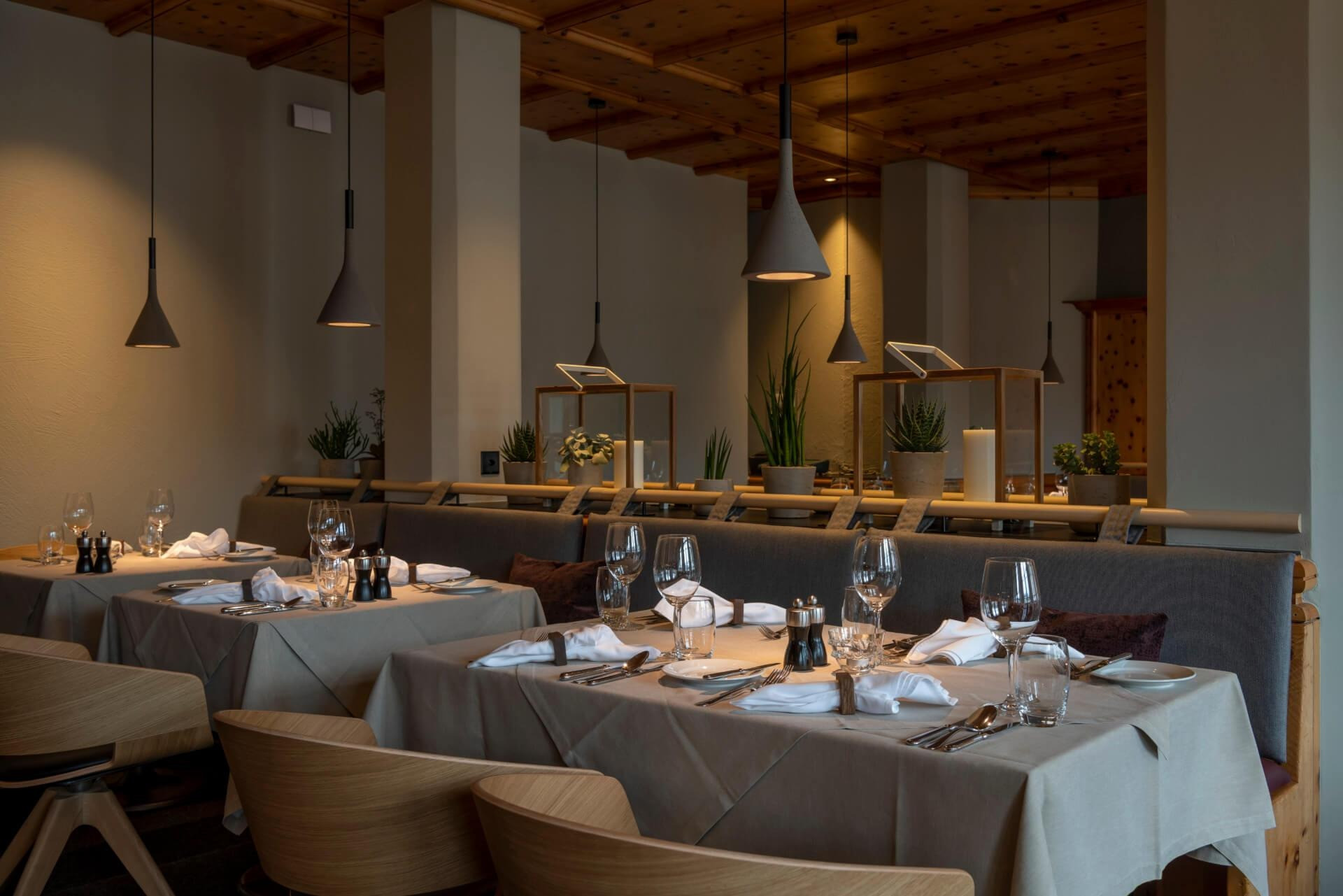 Elegantes Restaurant im Hotel Schweizerhof Lenzerheide mit modernem Alpenstil, gedeckten Tischen, stilvollen Hängelampen und gemütlicher Atmosphäre für ein hochwertiges Dinnererlebnis.