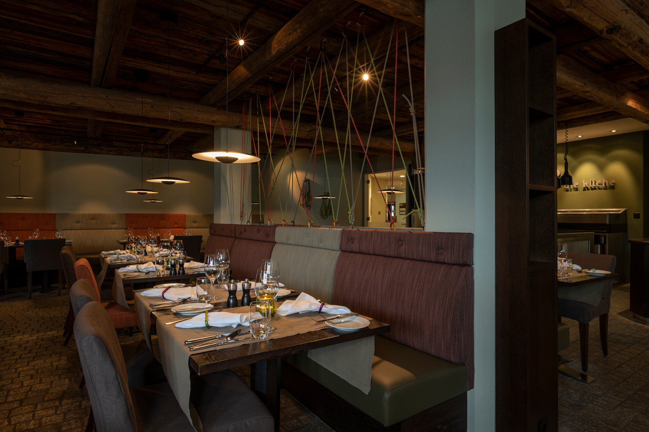 Stilvoll gedeckter Restaurantbereich im Hotel Schweizerhof mit Holzbalkendecke, gemütlichen Sitzbänken und modernem Ambiente.
