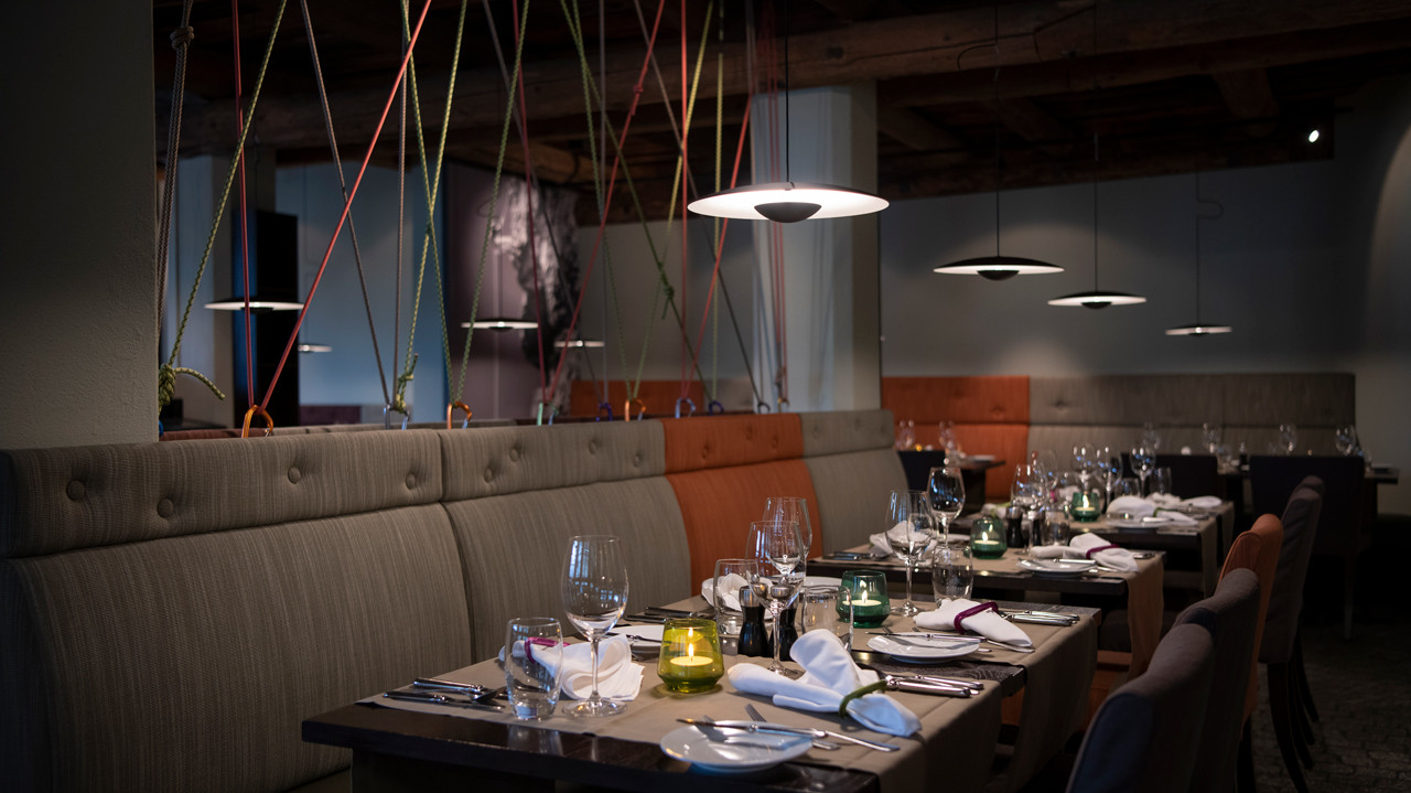Stilvoll gedeckter Restaurantbereich im Hotel Schweizerhof mit Holzbalkendecke, gemütlichen Sitzbänken und modernem Ambiente
