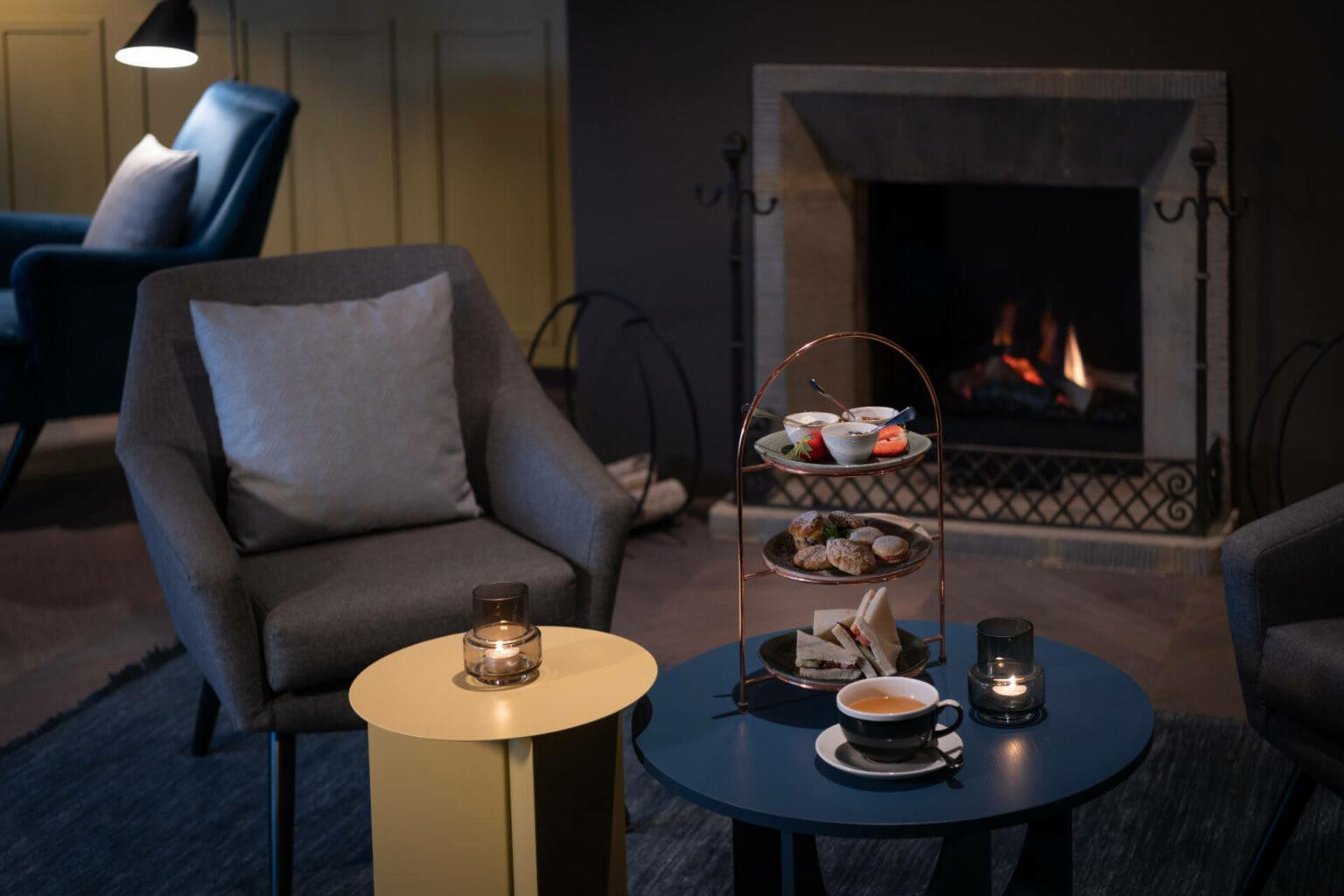 Sessel und Tisch mit Süssgebäck und Kaffee vor einem Kamin mit Feuer