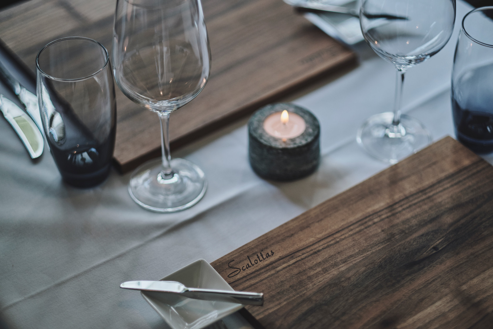 Nahaudnahme des Tisches mit einer Kerze und Weingläser und einer Holzunterlage mit einem Buttermesser und Butterschale daneben