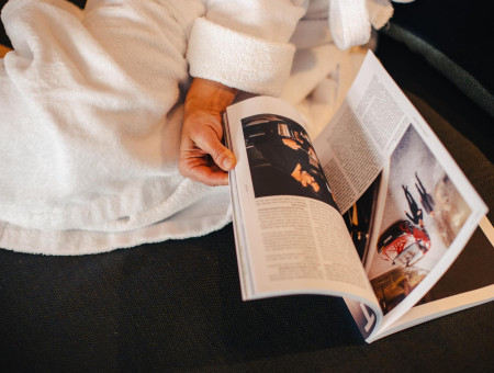 Gast im Hotel Schweizerhof Lenzerheide entspannt im Bademantel und liest eine Zeitschrift im Wellnessbereich