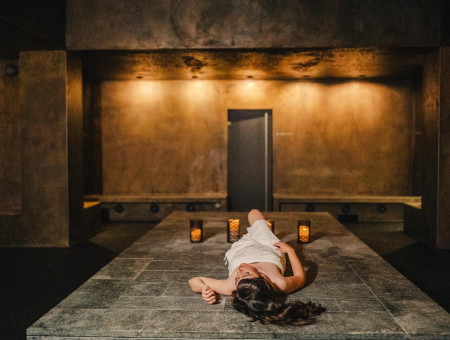 Frau ruht auf einer warmen Steinliege im Dampfbad des Hotel Schweizerhof Lenzerheide – entspannte Atmosphäre bei Kerzenschein im Wellnessbereich