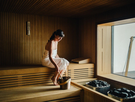 Frau entspannt in der Sauna des Hotel Schweizerhof Lenzerheide und genießt die wohltuende Wärme im modernen Wellnessbereich