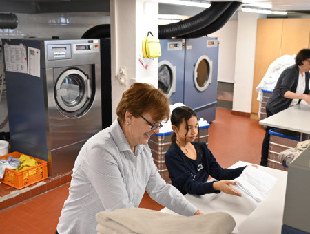 Teilnehmerin des Behind the Scenes Programms faltet Wäsche in der Hotel-Lingerie des Schweizerhof Lenzerheide unter Anleitung einer Mitarbeiterin