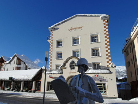 Winterliche Außenansicht des Altbauteils des Hotel Schweizerhof Lenzerheide mit verschneiter Fassade und markanter Statue im Vordergrund