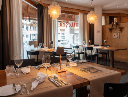 Restaurant Allegra im Hotel Schweizerhof Lenzerheide mit elegant gedeckten Tischen, stilvollen Lampen und Blick auf die Sonnenterrasse