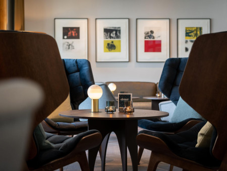 Gemütliche Lounge im Hotel Schweizerhof Lenzerheide mit stilvollen Sesseln, Kunst an den Wänden und warmem Licht für entspannte Atmosphäre