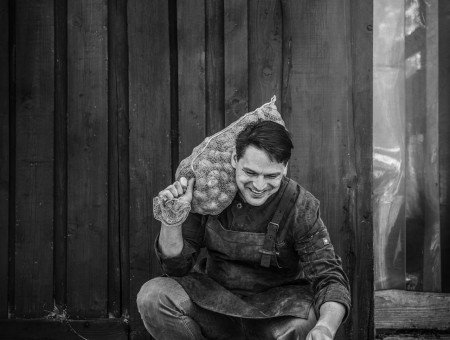Koch mit Kartoffelsack und Katze vor Holzscheune – bodenständige Handwerkskunst im Scalottas Terroir Lenzerheide