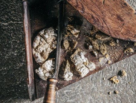 Zerbrochenes Brot mit Messer auf rustikalem Holzbrett – Symbol für ehrliche Handarbeit im Scalottas Terroir Lenzerheide