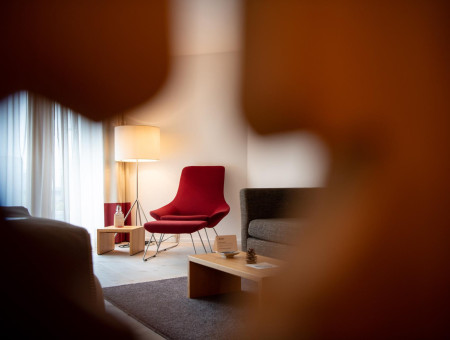 Modern eingerichtete Suite Alpenchic im Hotel Schweizerhof Lenzerheide mit rotem Designersessel und harmonischer Lichtstimmung