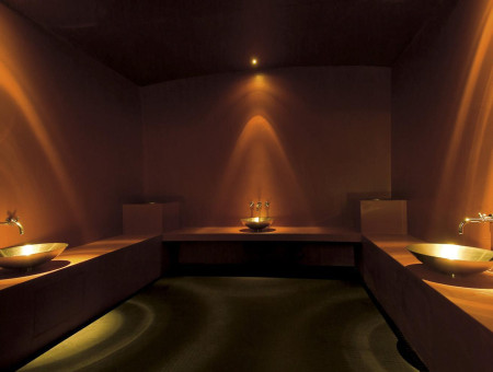 Stimmungsvoll beleuchteter Hamam im Wellnessbereich des Hotel Schweizerhof Lenzerheide mit goldfarbenen Waschschalen und warmem Lichtambiente