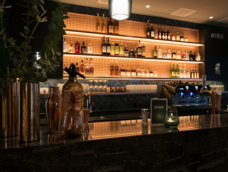 Design-Bar im Hotel Schweizerhof Lenzerheide mit eleganter Beleuchtung, hochwertigen Spirituosen und stilvoller Kupferdeko für genussvolle Abende