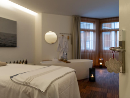 Behandlungsraum im Wellnessbereich des Hotel Schweizerhof Lenzerheide mit Massageliege, Badewanne und gemütlicher Beleuchtung für vollkommene Entspannung