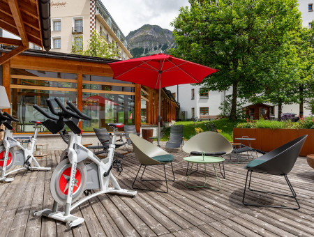 Hotel Schweizerhof Lenzerheide – Terrasse mit Fitnessrädern und Sitzlounge mit Blick auf die Bündner Berge