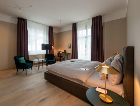 Geräumiges Nostalchic Zimmer im Hotel Schweizerhof Lenzerheide mit Kingsize-Bett, Sitzbereich und warmem Licht für entspannte Stunden