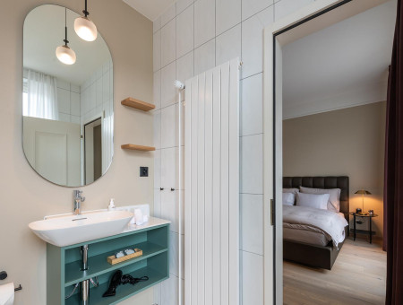 Modernes Badezimmer im Nostalchic Zimmer des Hotel Schweizerhof Lenzerheide mit großem Spiegel, eleganter Ausstattung und Blick ins Schlafzimmer