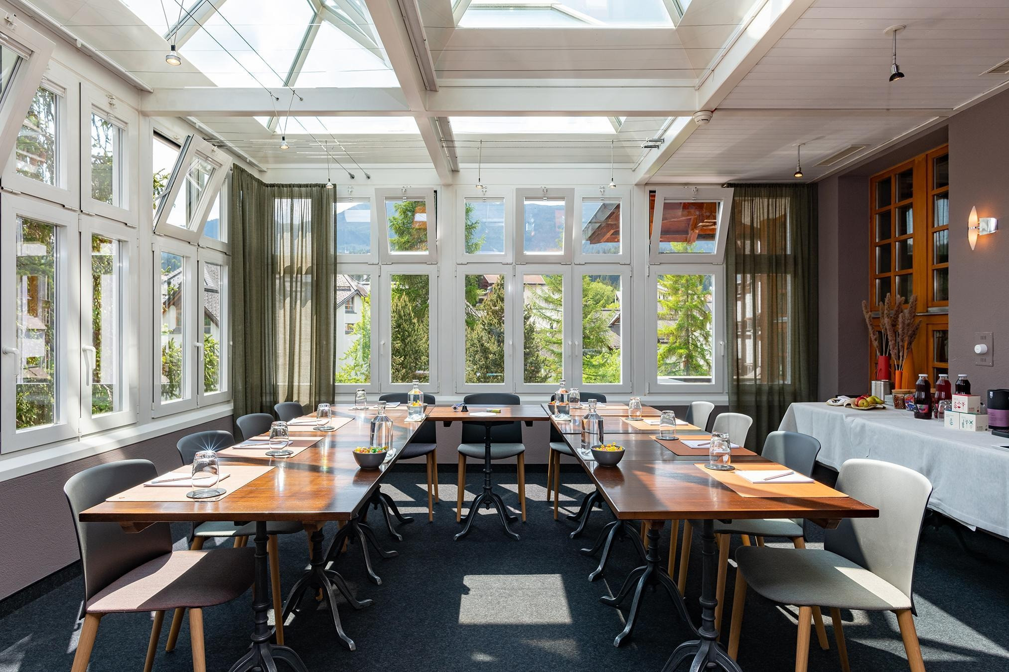 Wintergarten mit Tischen und Stühlen. Auf den Tischen sind Gläser, Wasserflaschen und Schreibblöcke mit Stiften.