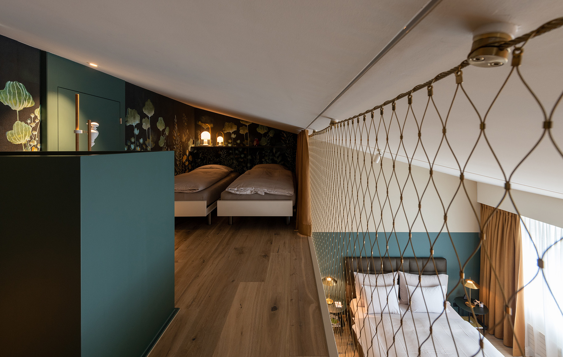 Nostalchic Hotelzimmer mit Galerie, zwei Einzelbetten unter schräger Decke und floralem Wanddesign sowie Blick auf das darunterliegende Doppelbett durch ein dekoratives Sicherheitsnetz.