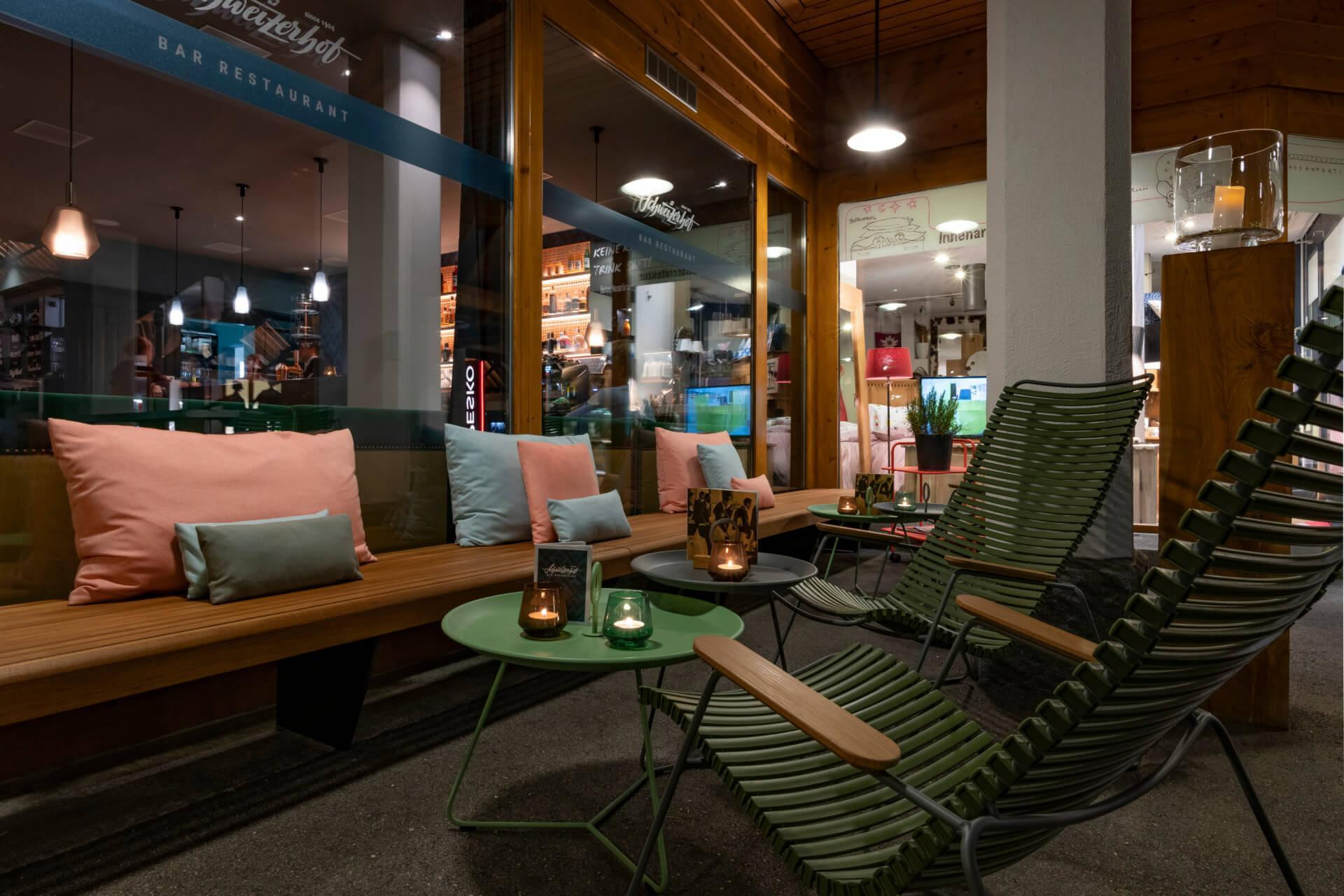 Aussenlounge mit Sitzbank und Liegestühlen. Beistellstische mit Kerzen und Speise und Getränkekarten