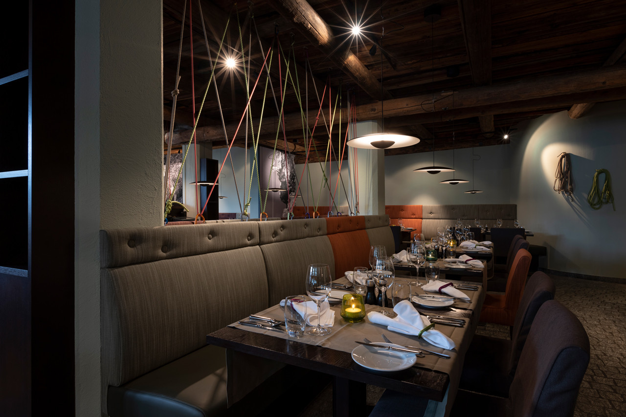 Stilvoll gedeckter Restaurantbereich im Hotel Schweizerhof mit Holzbalkendecke, gemütlichen Sitzbänken und modernem Ambiente.