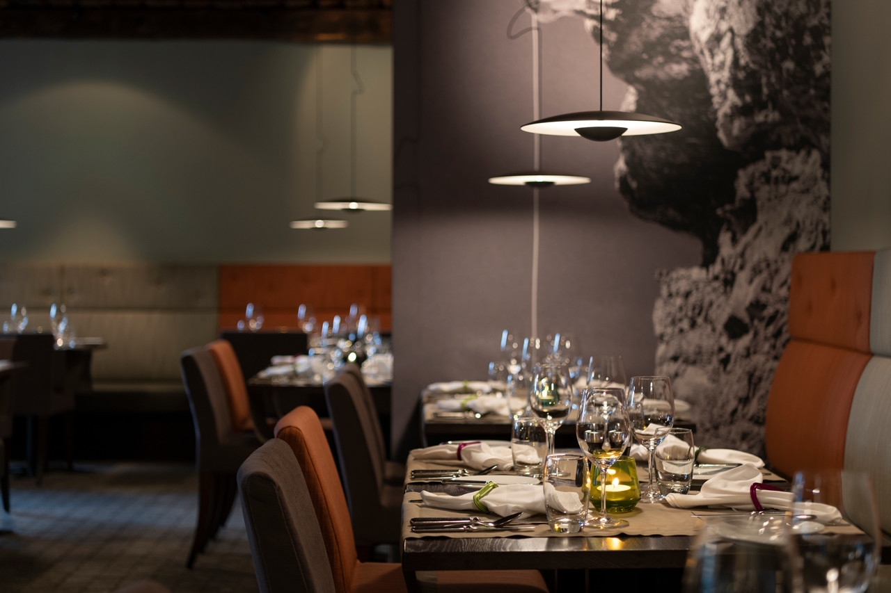 Elegantes Restaurant im Hotel Schweizerhof Lenzerheide mit modernem Alpenstil, gedeckten Tischen, stilvollen Hängelampen.