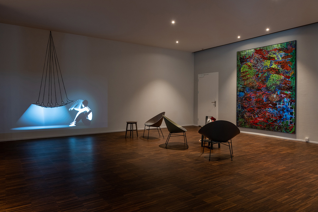 Moderner Kunstraum im Hotel Schweizerhof Lenzerheide mit Videoprojektion, Designer-Loungestühlen und grossformatigem, farbenfrohem Gemälde für kulturelle Inspiration.