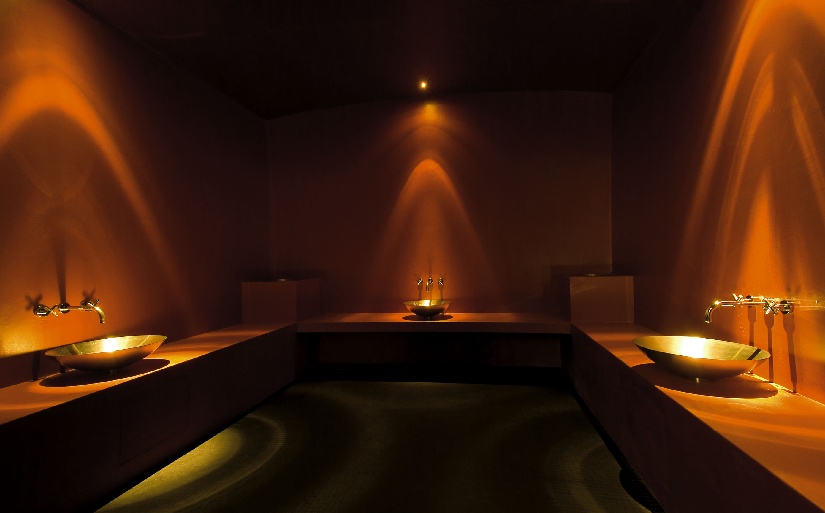 Atmosphärischer Hamam-Bereich im Hotel Schweizerhof Lenzerheide mit warmem, goldenem Licht, modernen Waschschalen und ruhiger Wellness­stimmung.