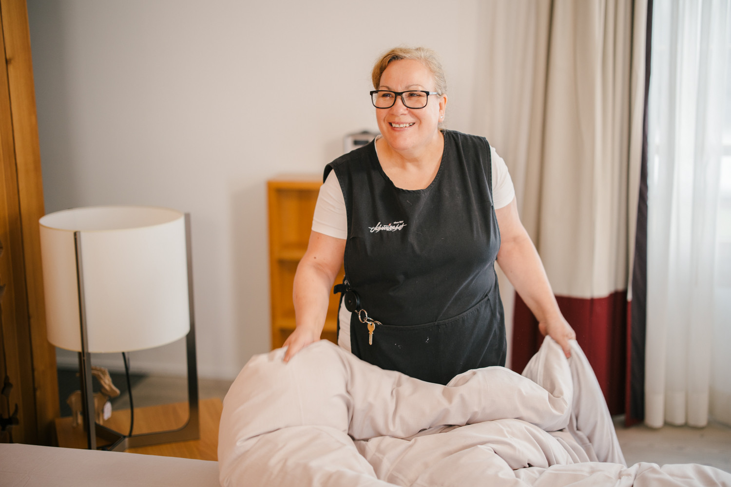 Mitarbeiterin der Reinigung bettet gerade ein Bett in einem der Hotelzimmer.