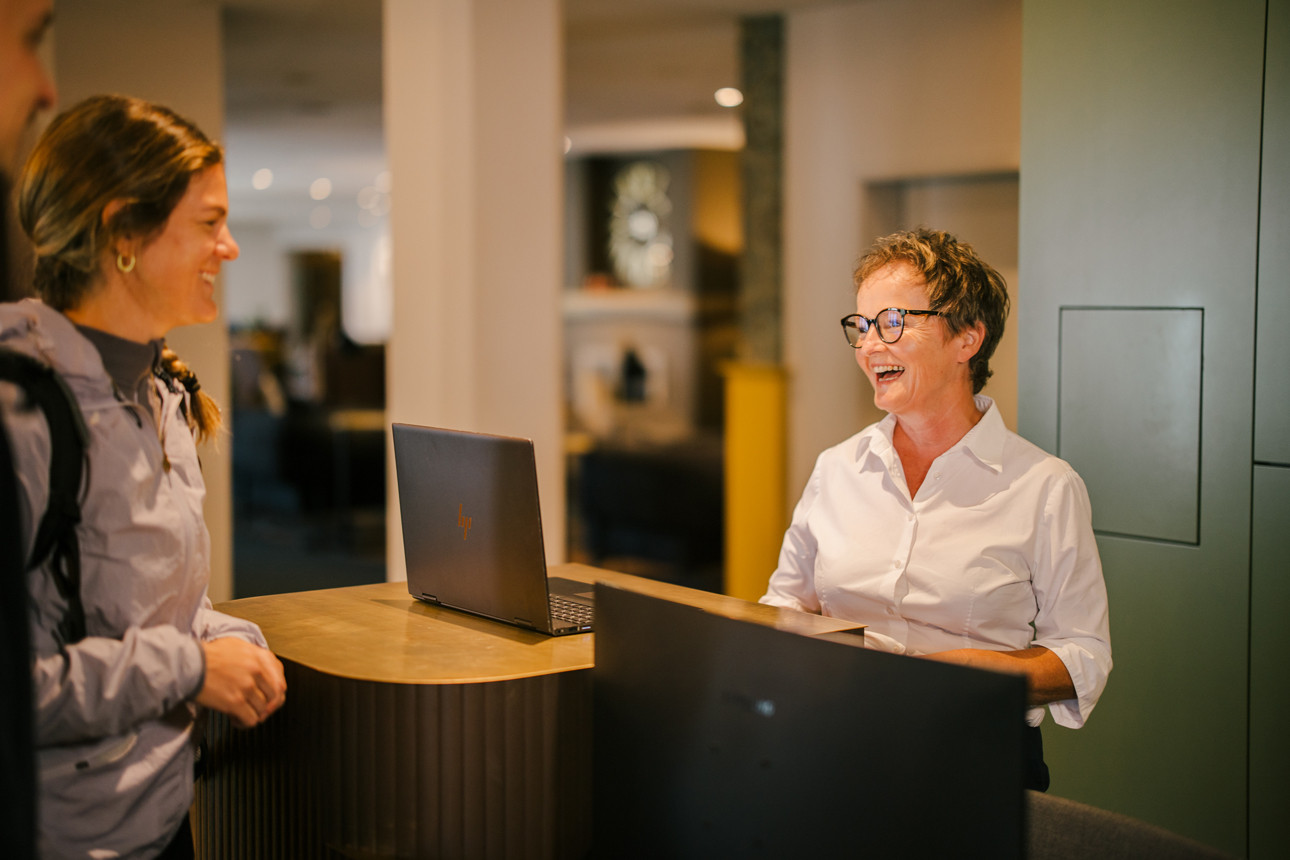 Rezeptionistin berät eine Kundin freundlich im Hotel-Loungebereich.