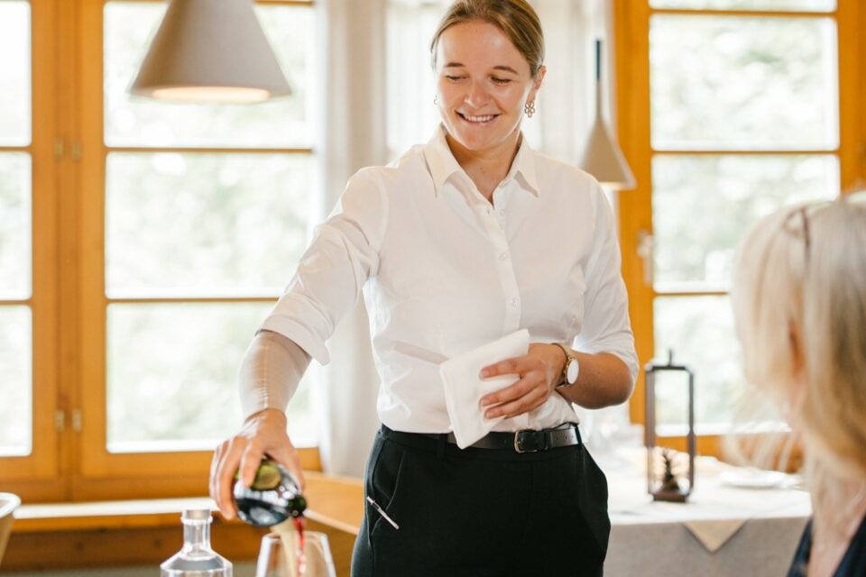 Mitarbeiterin im Service die gerade einer Kundin Wein einschenkt.