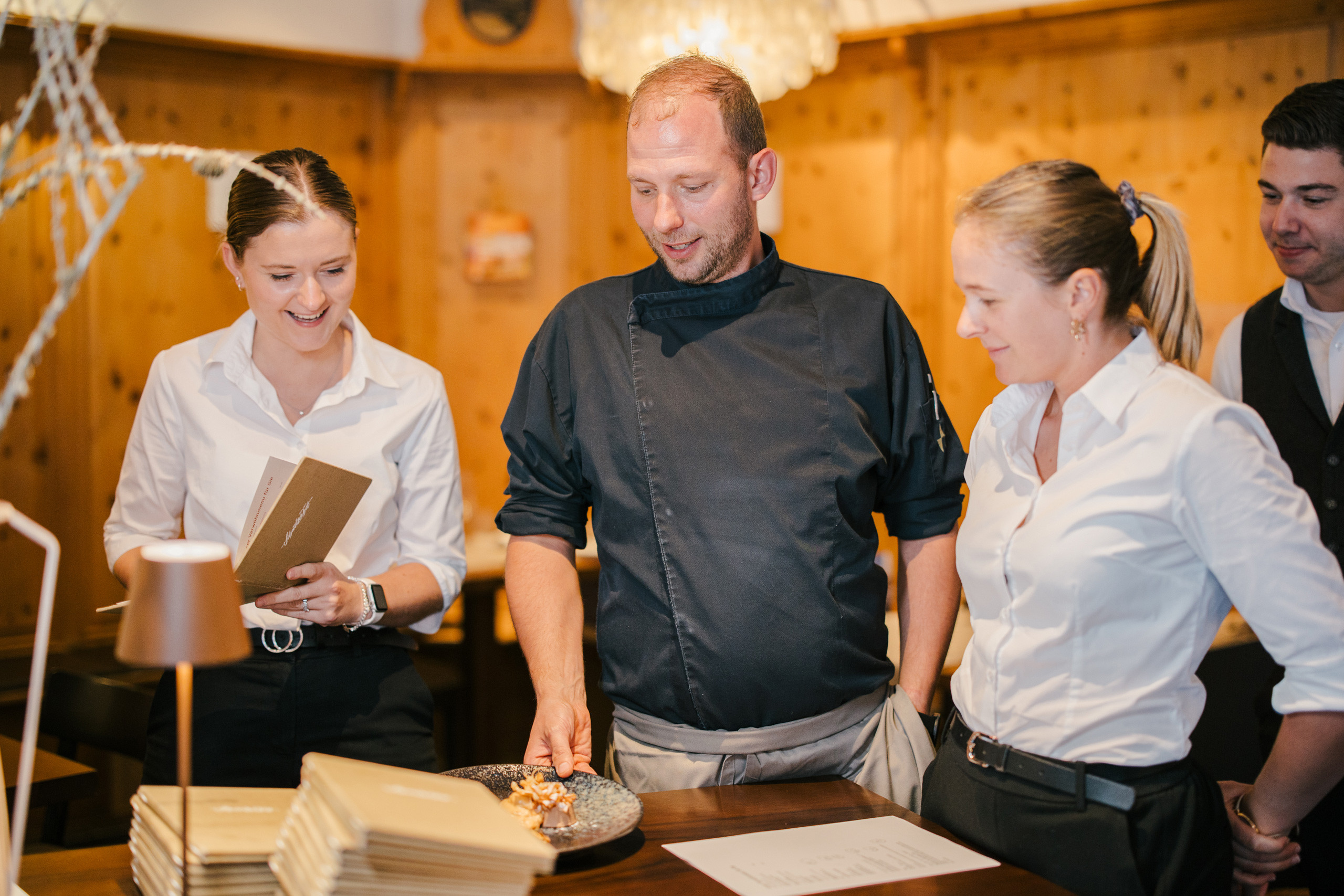 Mehrere Mitarbeiter des Service-Teams und ein Koch der ein Teller mit Essen hält unterhalten sich.
