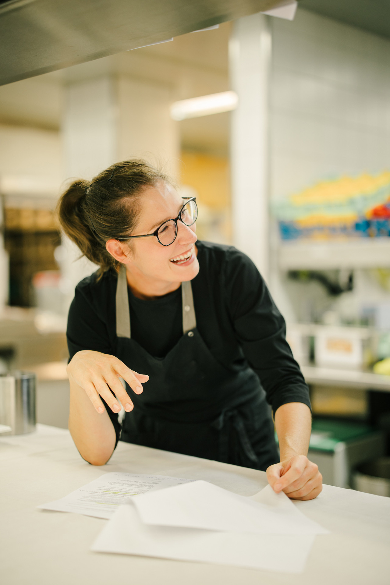 Mitarbeiterin in der Küche lachend während sie ein Dokument liest.